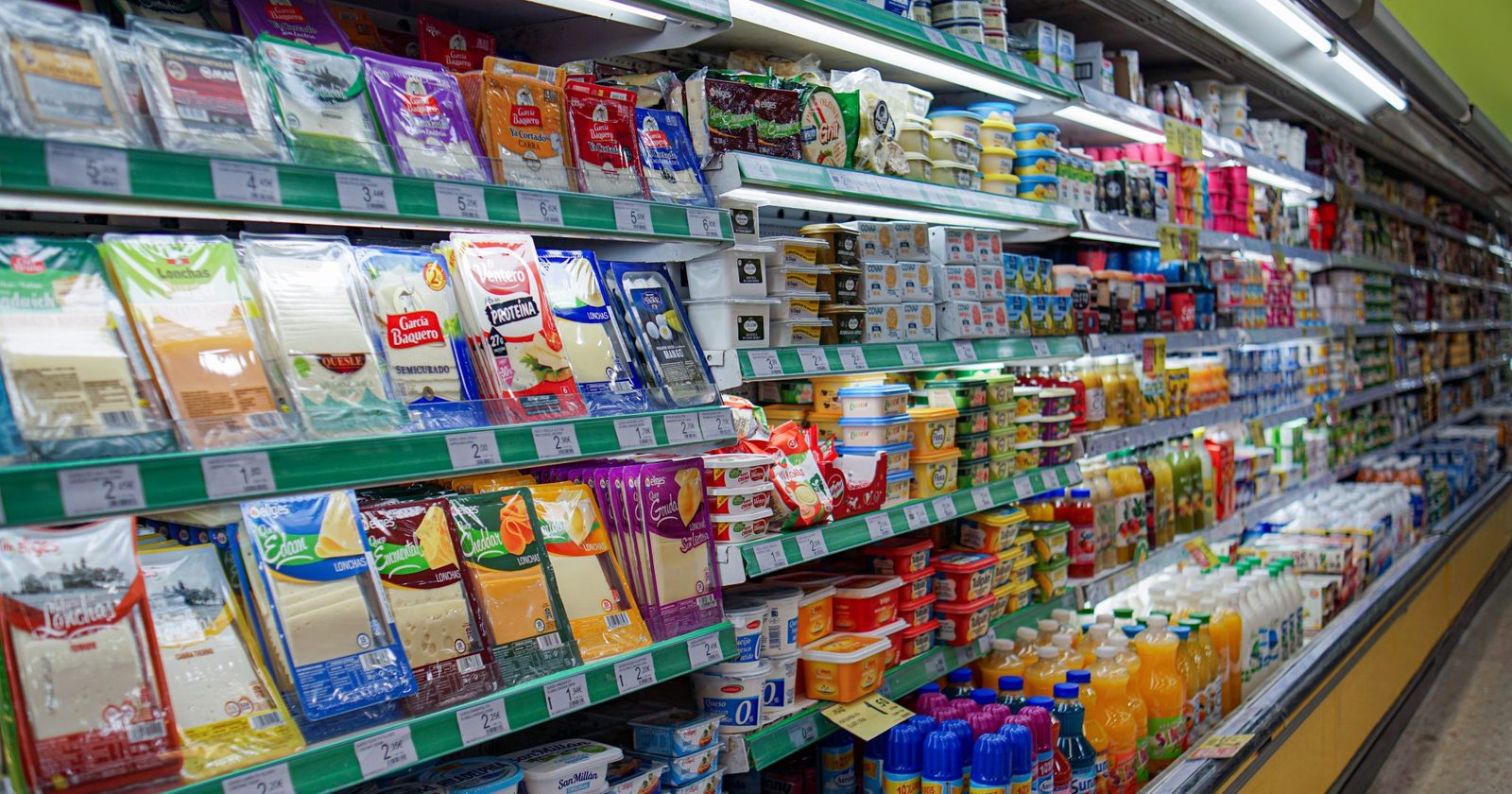 Alejka supermarketu z półkami pełnymi nabiału i napojów oraz widocznymi etykietami cenowymi.