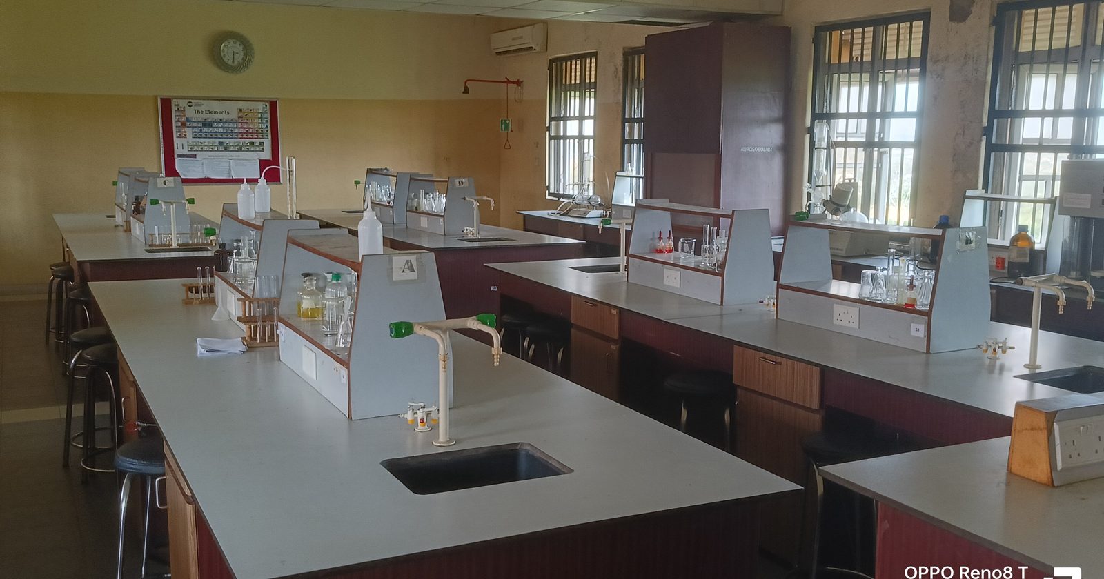 Wnętrze pracowni chemicznej: rzędy stołów laboratoryjnych ze zlewami, statywami i szkłem laboratoryjnym.